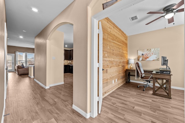 office with visible vents, light wood-style flooring, arched walkways, wooden walls, and ceiling fan