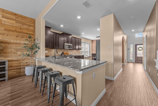 kitchen with light stone counters, visible vents, a breakfast bar, decorative backsplash, and stainless steel microwave