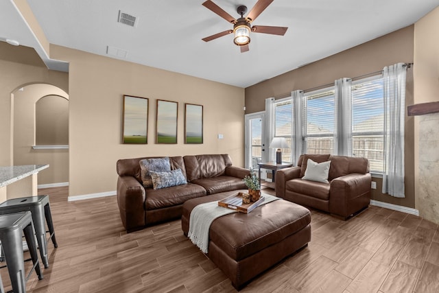 living area featuring arched walkways, visible vents, a ceiling fan, and light wood-style floors