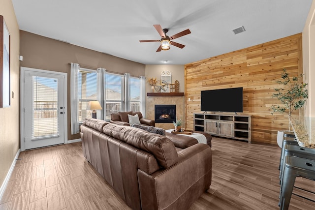 living area featuring light wood-type flooring, visible vents, wooden walls, ceiling fan, and a tile fireplace