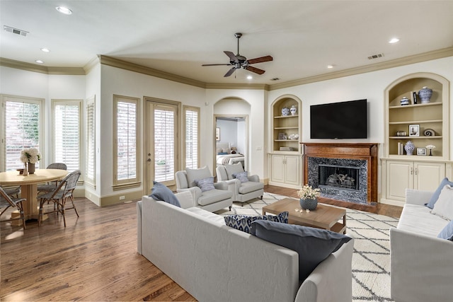 living room featuring built in features, wood finished floors, visible vents, and a premium fireplace