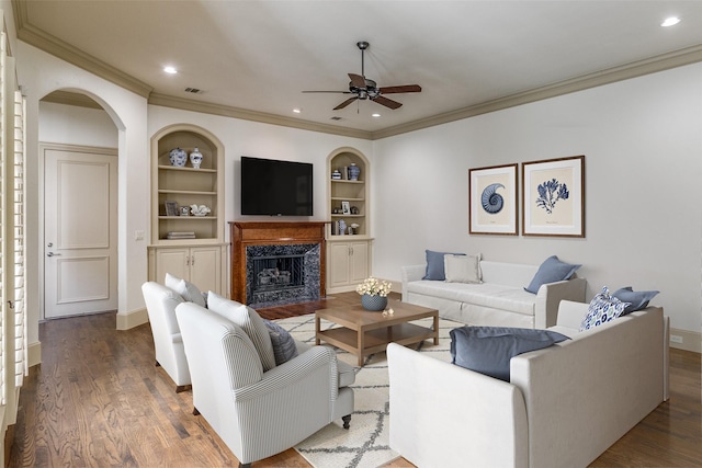 living room featuring built in features, wood finished floors, visible vents, baseboards, and a high end fireplace