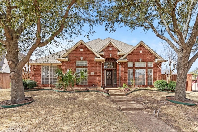 view of front facade featuring brick siding, a shingled roof, and fence