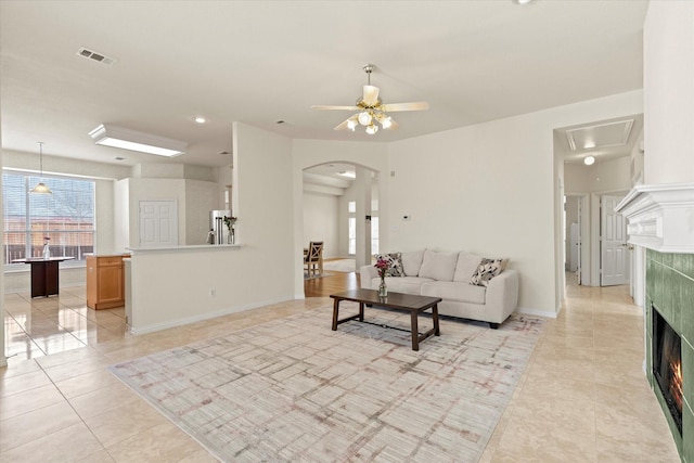 living room featuring visible vents, a ceiling fan, arched walkways, a fireplace, and light tile patterned floors