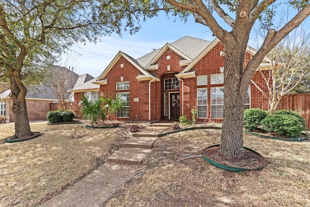 view of front of home with brick siding, a shingled roof, and fence