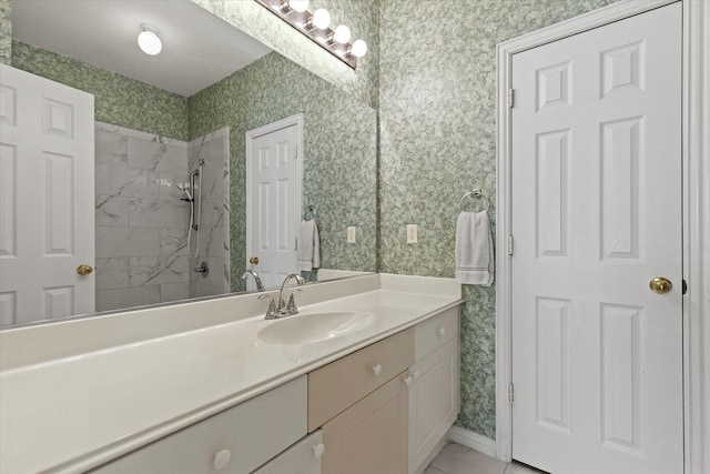 bathroom featuring tiled shower, wallpapered walls, vanity, and baseboards