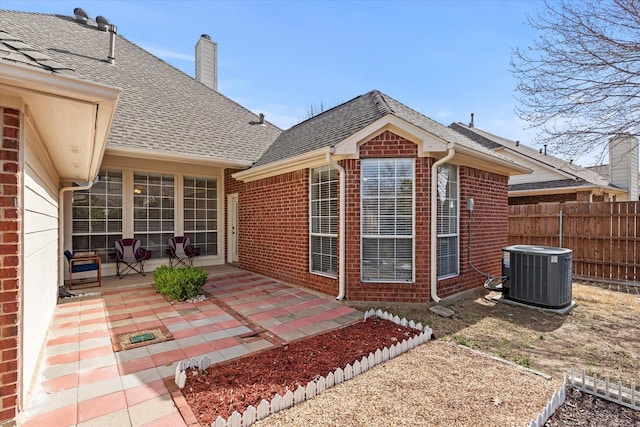 exterior space with central AC unit, fence, roof with shingles, a patio area, and brick siding