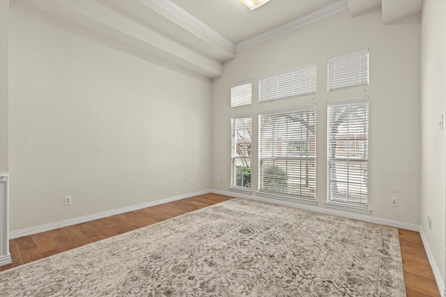 empty room with wood finished floors, baseboards, and ornamental molding