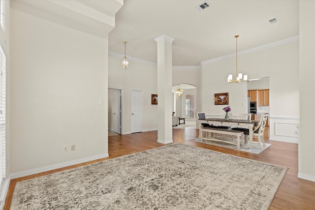 living area with visible vents, ornate columns, a high ceiling, ornamental molding, and light wood-style floors