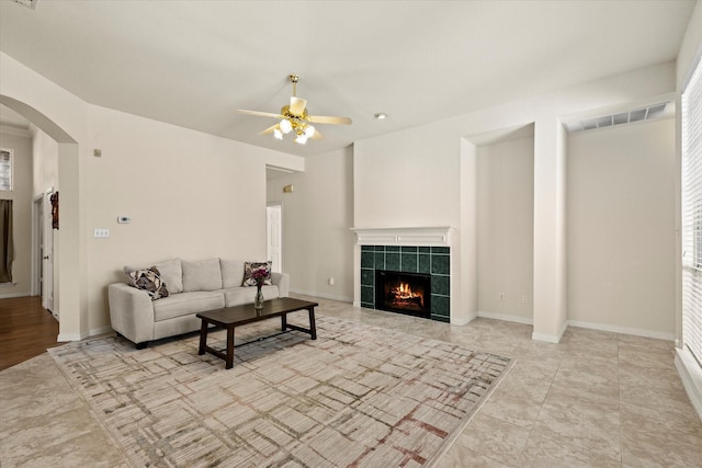 living area featuring visible vents, baseboards, ceiling fan, a fireplace, and arched walkways