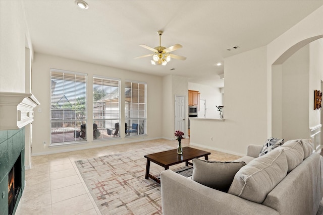 living room featuring visible vents, a ceiling fan, a tiled fireplace, arched walkways, and light tile patterned flooring