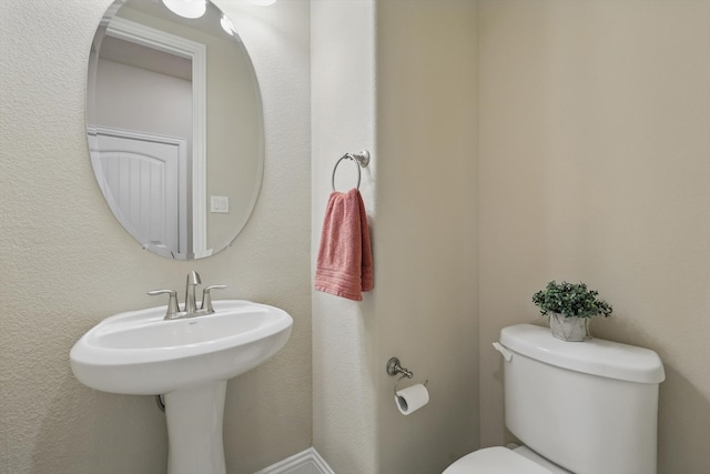 bathroom featuring toilet, a textured wall, and a sink