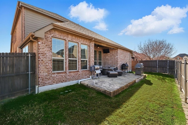 rear view of house with brick siding, a patio area, a yard, and a fenced backyard