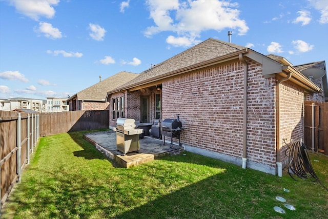 rear view of property with a patio, a yard, a fenced backyard, and brick siding