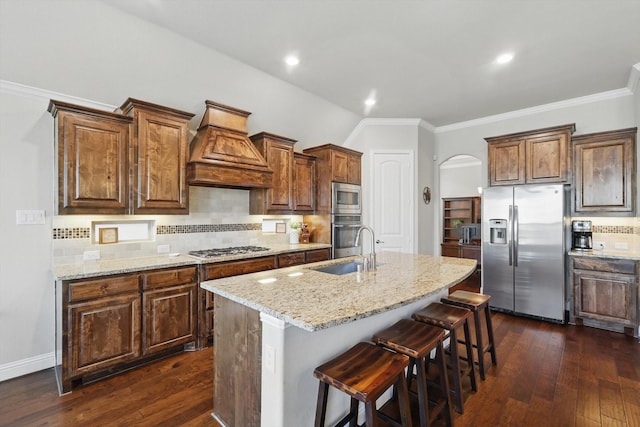 kitchen featuring light stone counters, arched walkways, a sink, stainless steel appliances, and custom range hood