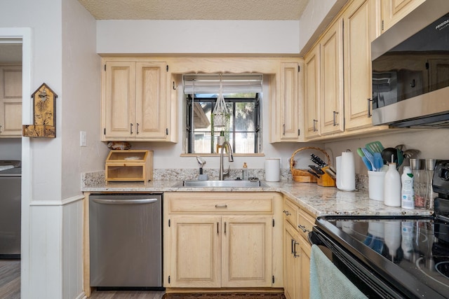 kitchen with a wainscoted wall, light brown cabinets, stainless steel appliances, and a sink