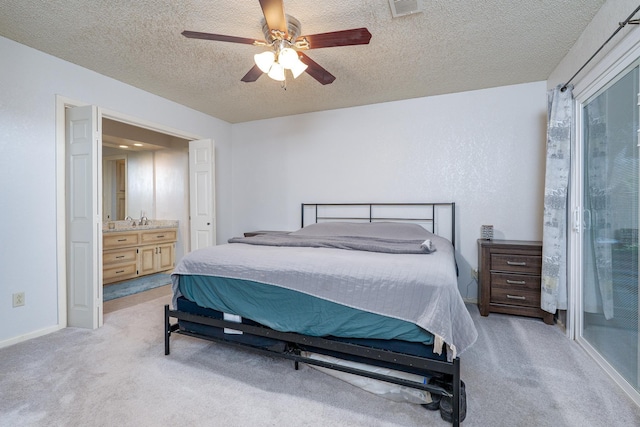 bedroom featuring baseboards, ceiling fan, ensuite bathroom, a textured ceiling, and light colored carpet