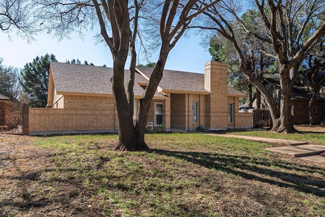 ranch-style home featuring fence, roof with shingles, a front yard, brick siding, and a chimney