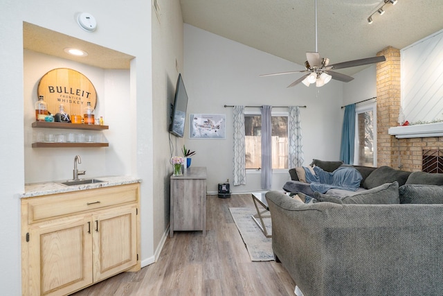 living area with a textured ceiling, light wood-style floors, wet bar, a brick fireplace, and ceiling fan