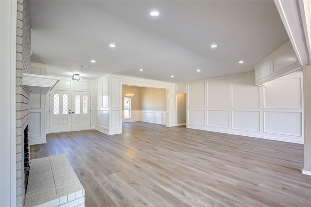 unfurnished living room with visible vents, a brick fireplace, a decorative wall, light wood-type flooring, and recessed lighting