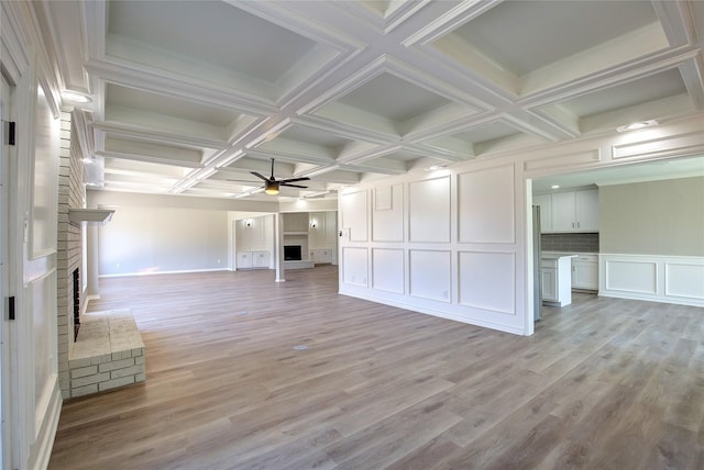 unfurnished living room with a brick fireplace, a decorative wall, beamed ceiling, light wood-type flooring, and a ceiling fan