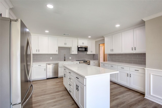 kitchen with crown molding, appliances with stainless steel finishes, light wood finished floors, and a sink