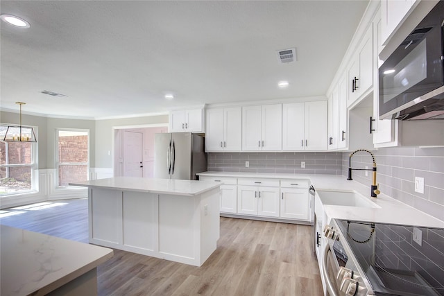 kitchen featuring visible vents, a center island, light wood-type flooring, a sink, and stainless steel appliances