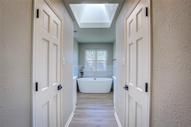corridor featuring a skylight, a textured wall, and wood finished floors