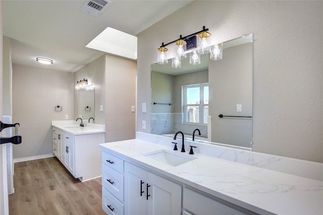 bathroom with a sink, two vanities, wood finished floors, and visible vents