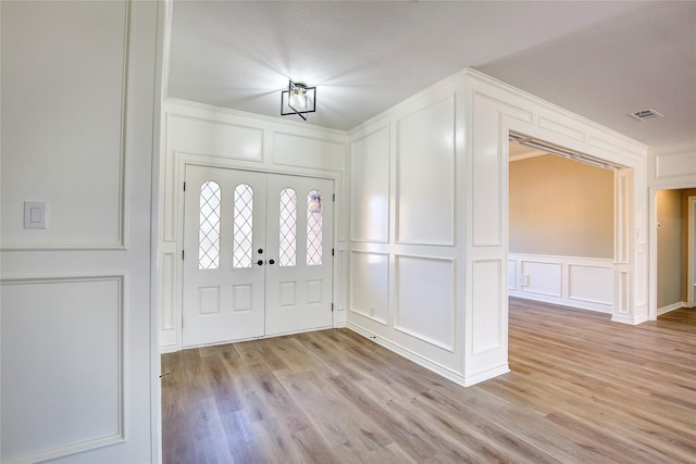 entryway featuring visible vents, light wood-type flooring, french doors, and a decorative wall