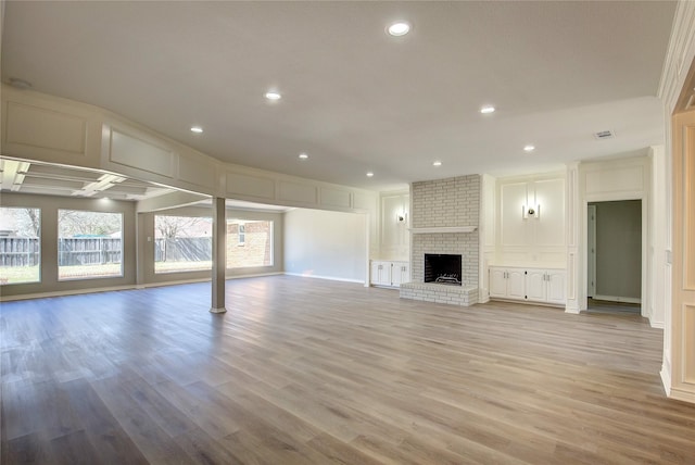 unfurnished living room featuring a brick fireplace, recessed lighting, light wood-style flooring, and a decorative wall