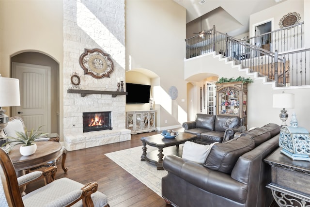 living room featuring wood finished floors, stairway, arched walkways, a high ceiling, and a stone fireplace