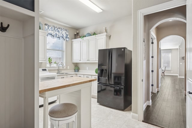 kitchen with butcher block counters, a kitchen bar, black refrigerator with ice dispenser, arched walkways, and a sink