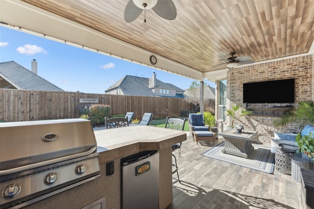 view of patio / terrace featuring grilling area, an outdoor living space with a fireplace, a fenced backyard, and exterior kitchen