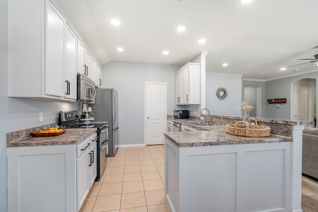 kitchen with appliances with stainless steel finishes, a peninsula, arched walkways, white cabinetry, and a sink