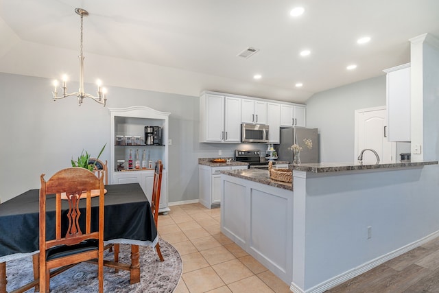 kitchen featuring visible vents, dark stone counters, a peninsula, appliances with stainless steel finishes, and white cabinets