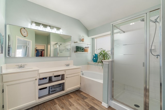 bathroom with a stall shower, a sink, wood finished floors, a bath, and vaulted ceiling