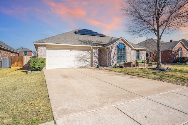 single story home with brick siding, solar panels, concrete driveway, and a front lawn