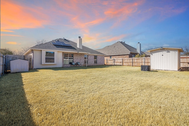 back of house at dusk with a yard, a storage unit, a fenced backyard, and an outdoor structure