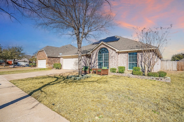 ranch-style home featuring roof mounted solar panels, a yard, concrete driveway, a garage, and brick siding