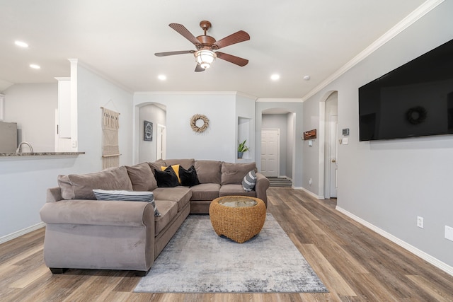 living room featuring arched walkways, ornamental molding, baseboards, and wood finished floors