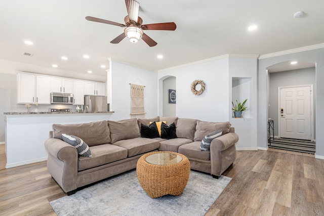 living area featuring visible vents, light wood-style flooring, ornamental molding, arched walkways, and baseboards