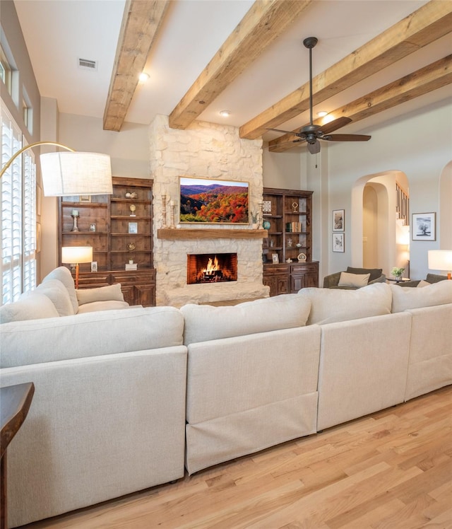 living area with a ceiling fan, wood finished floors, visible vents, a fireplace, and arched walkways