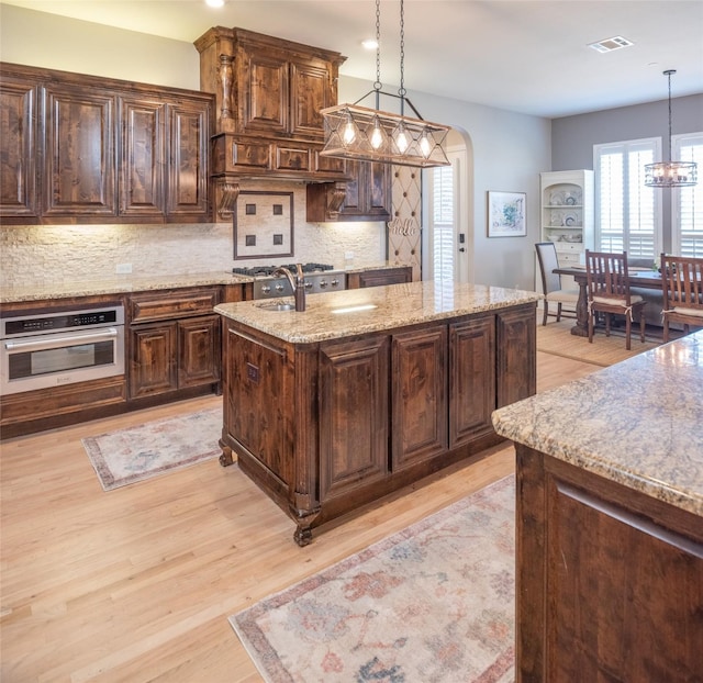 kitchen with arched walkways, stainless steel appliances, hanging light fixtures, decorative backsplash, and light wood-type flooring