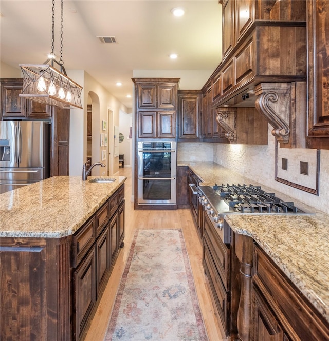 kitchen with visible vents, arched walkways, a sink, stainless steel appliances, and tasteful backsplash