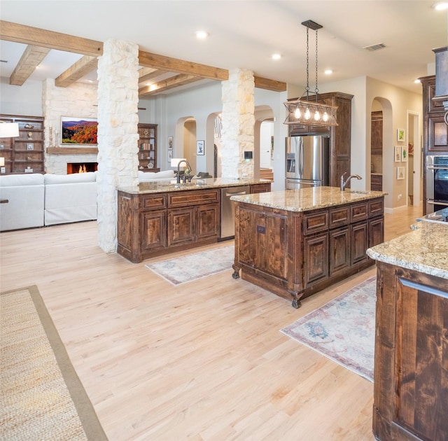 kitchen with open floor plan, stainless steel appliances, arched walkways, light wood finished floors, and decorative columns