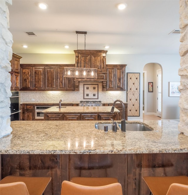 kitchen with light stone countertops, visible vents, arched walkways, a sink, and decorative backsplash