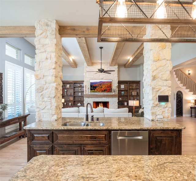 kitchen with a sink, a large fireplace, open floor plan, ornate columns, and stainless steel dishwasher