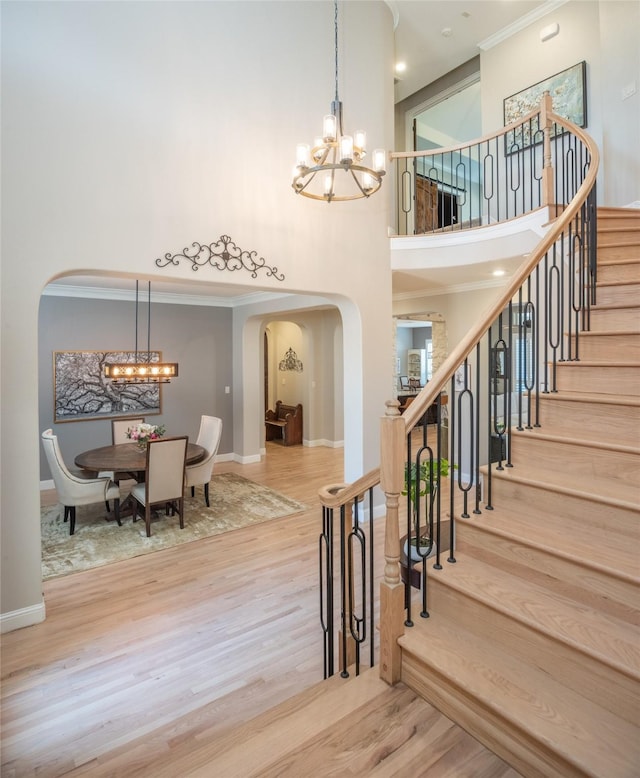 stairway with an inviting chandelier, wood finished floors, arched walkways, and a towering ceiling