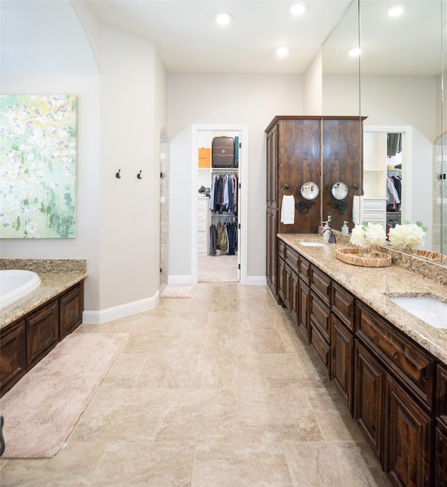 bathroom with double vanity, a walk in closet, a garden tub, and a sink